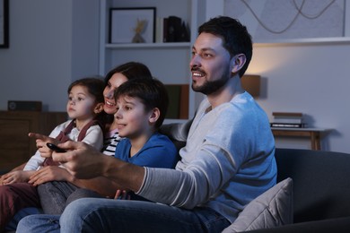 Photo of Happy family watching TV at home in evening. Father changing channels with remote control