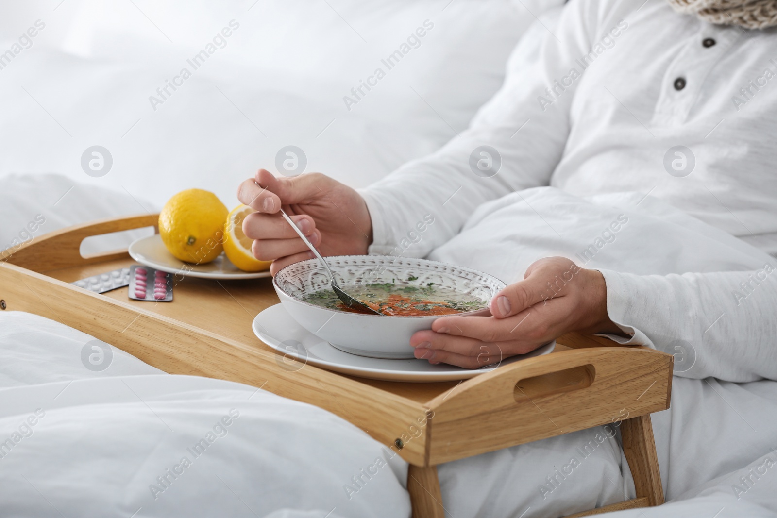 Photo of Sick young man eating soup to cure flu in bed at home, closeup