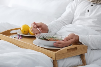 Photo of Sick young man eating soup to cure flu in bed at home, closeup