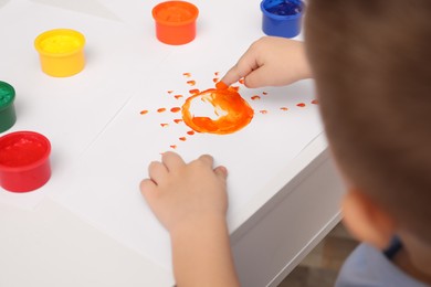 Photo of Little boy painting with finger at white table indoors, closeup