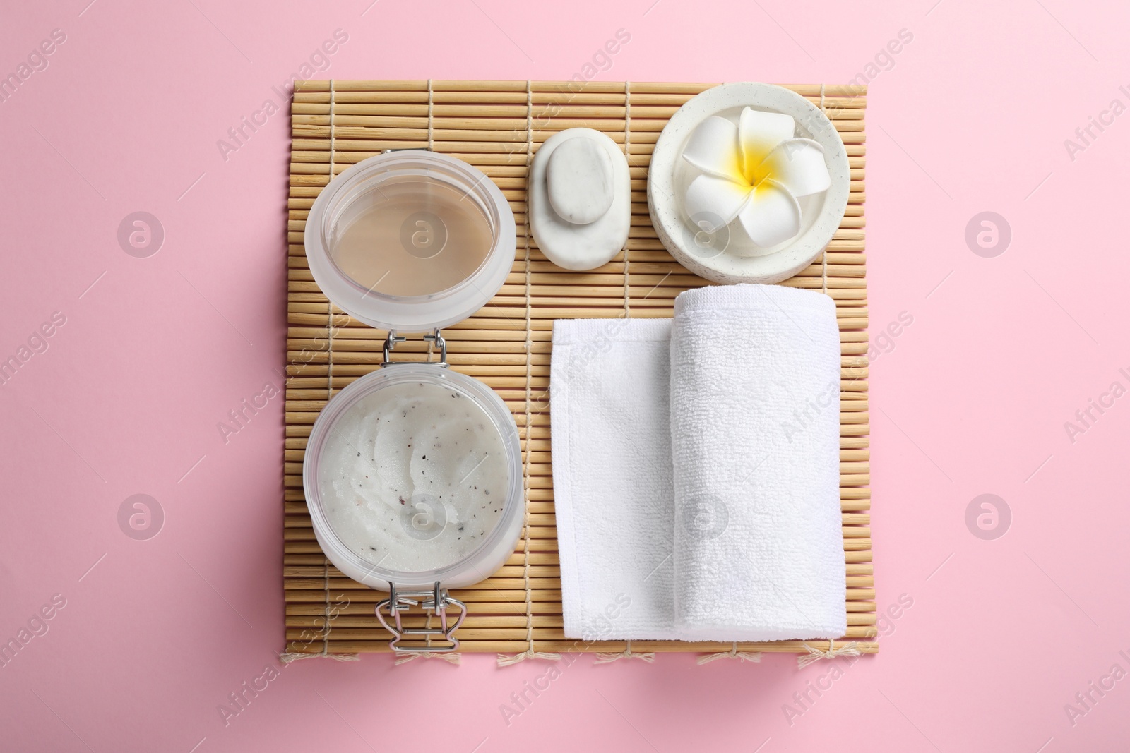 Photo of Body scrub, towel, spa stones and plumeria flower on pink background, top view