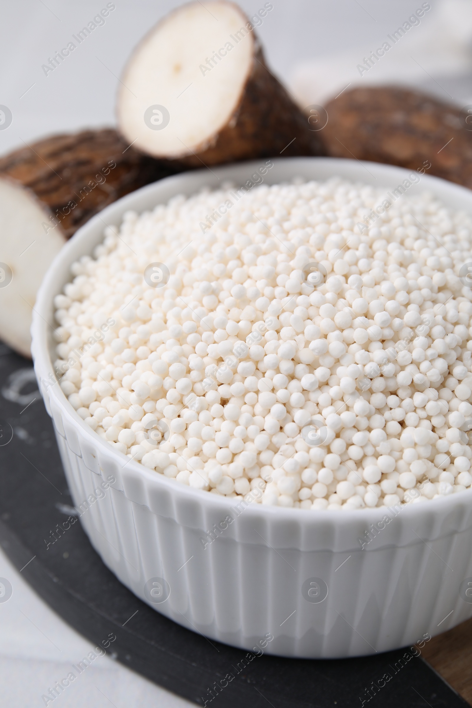 Photo of Tapioca pearls in bowl and cassava roots on table, closeup