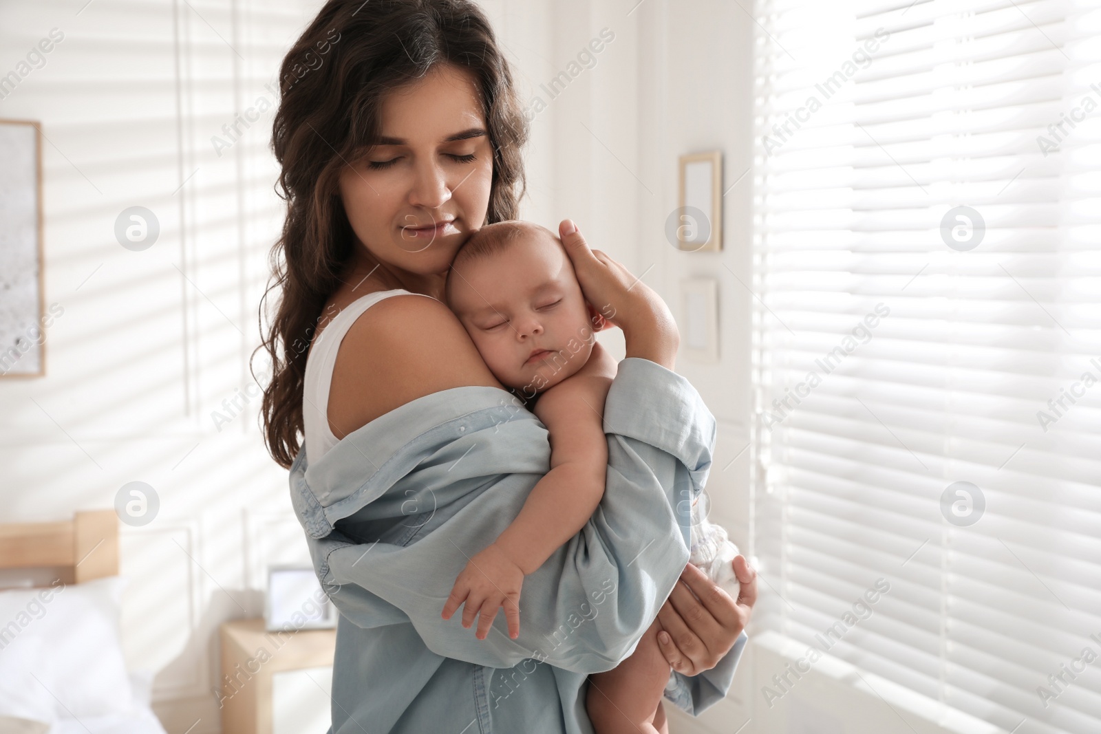 Photo of Happy young mother with her sleeping baby near window at home