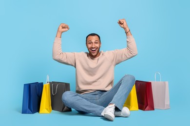 Photo of Happy African American man with shopping bags on light blue background