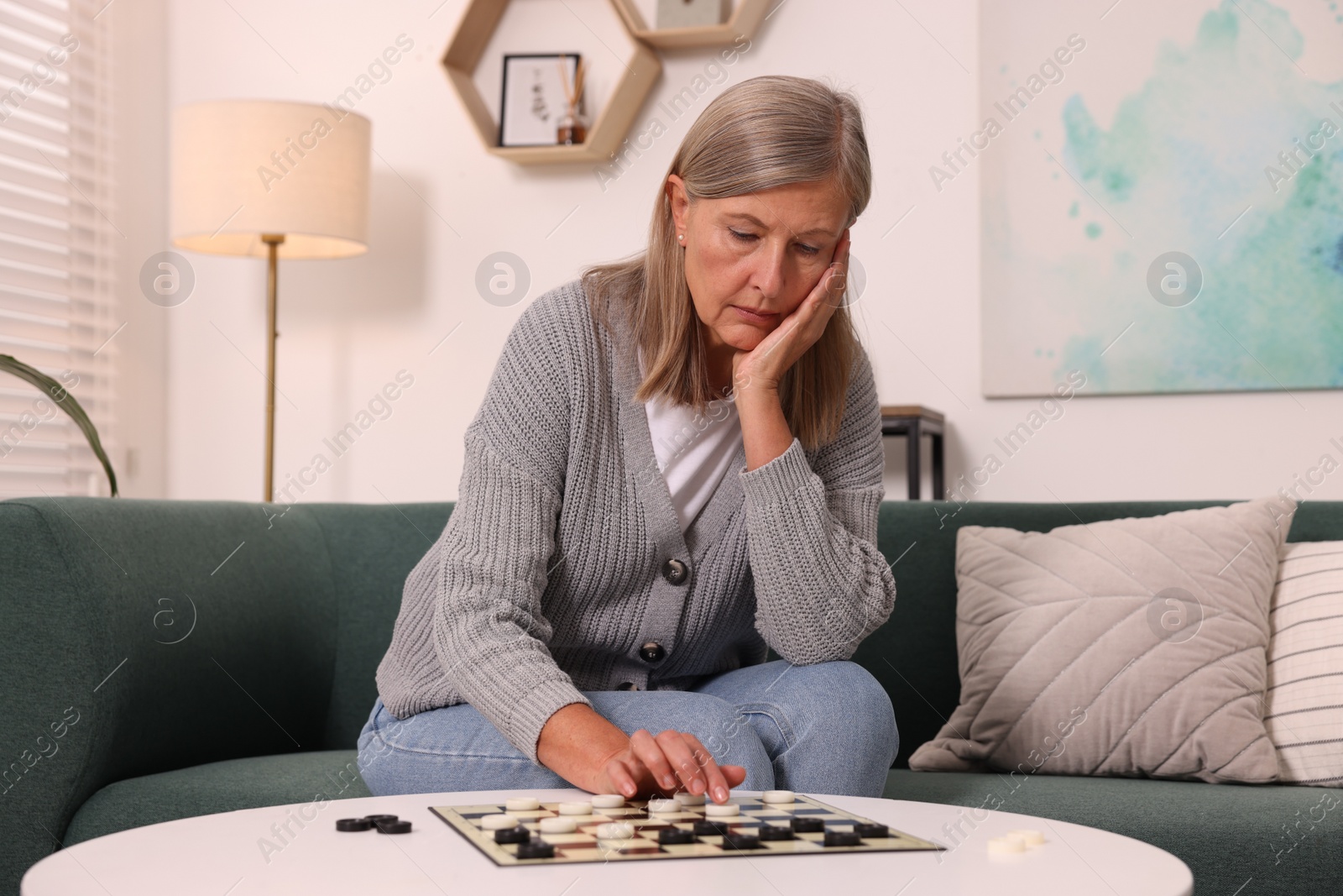 Photo of Thoughtful senior woman playing checkers at home
