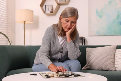 Thoughtful senior woman playing checkers at home