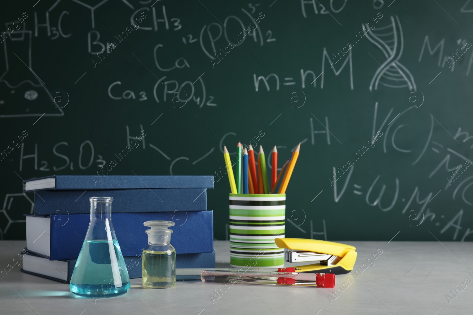 Photo of Laboratory glassware and school supplies on table against blackboard with chemical formulas