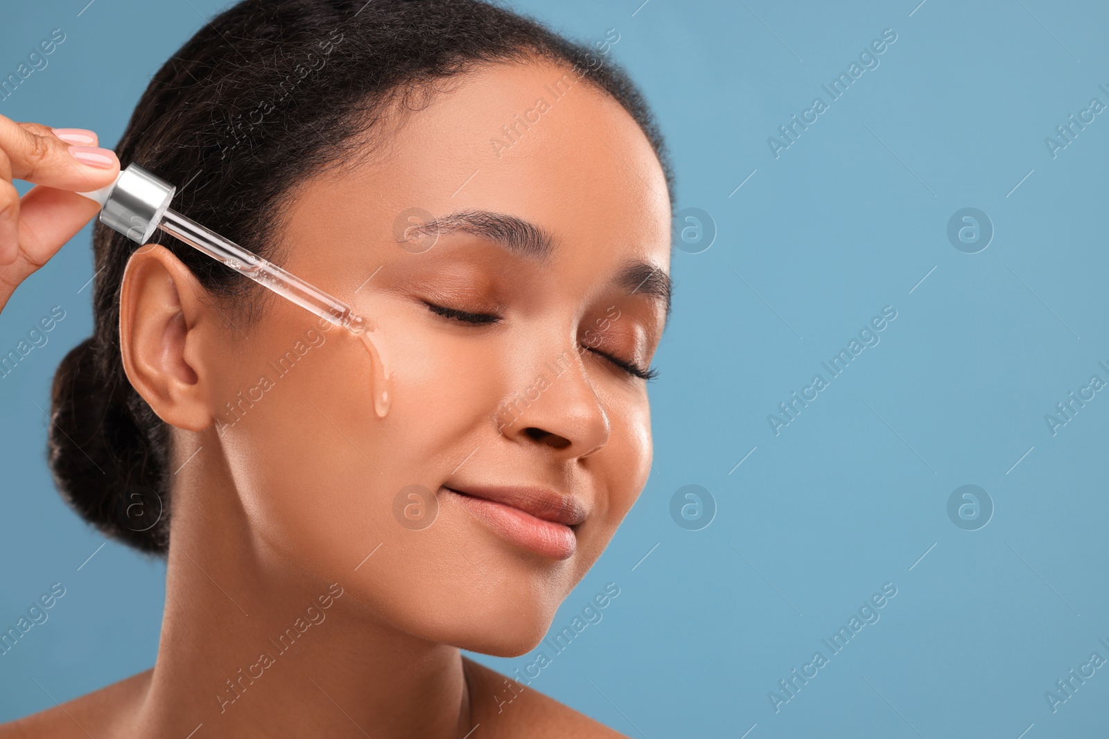 Photo of Beautiful woman applying serum onto her face on blue background, closeup. Space for text