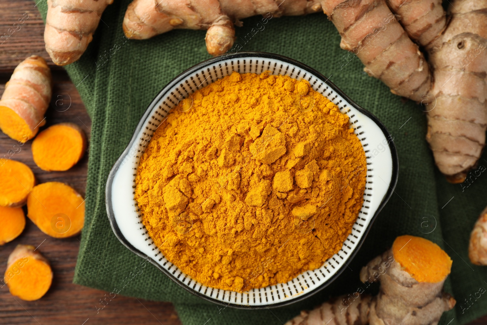 Photo of Bowl with aromatic turmeric powder and cut roots on table, flat lay