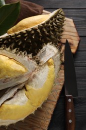 Pieces of fresh ripe durian and knife on black wooden table, top view