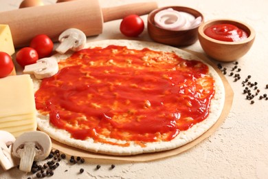 Photo of Pizza base smeared with tomato sauce, peppercorns and products on light textured table, closeup