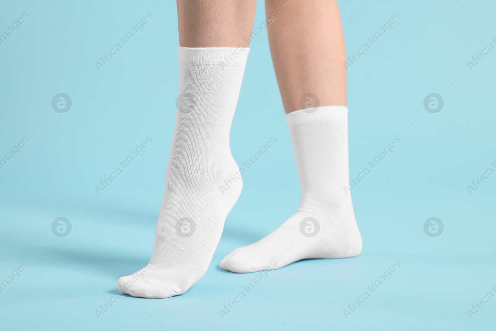 Photo of Woman in stylish white socks on light blue background, closeup