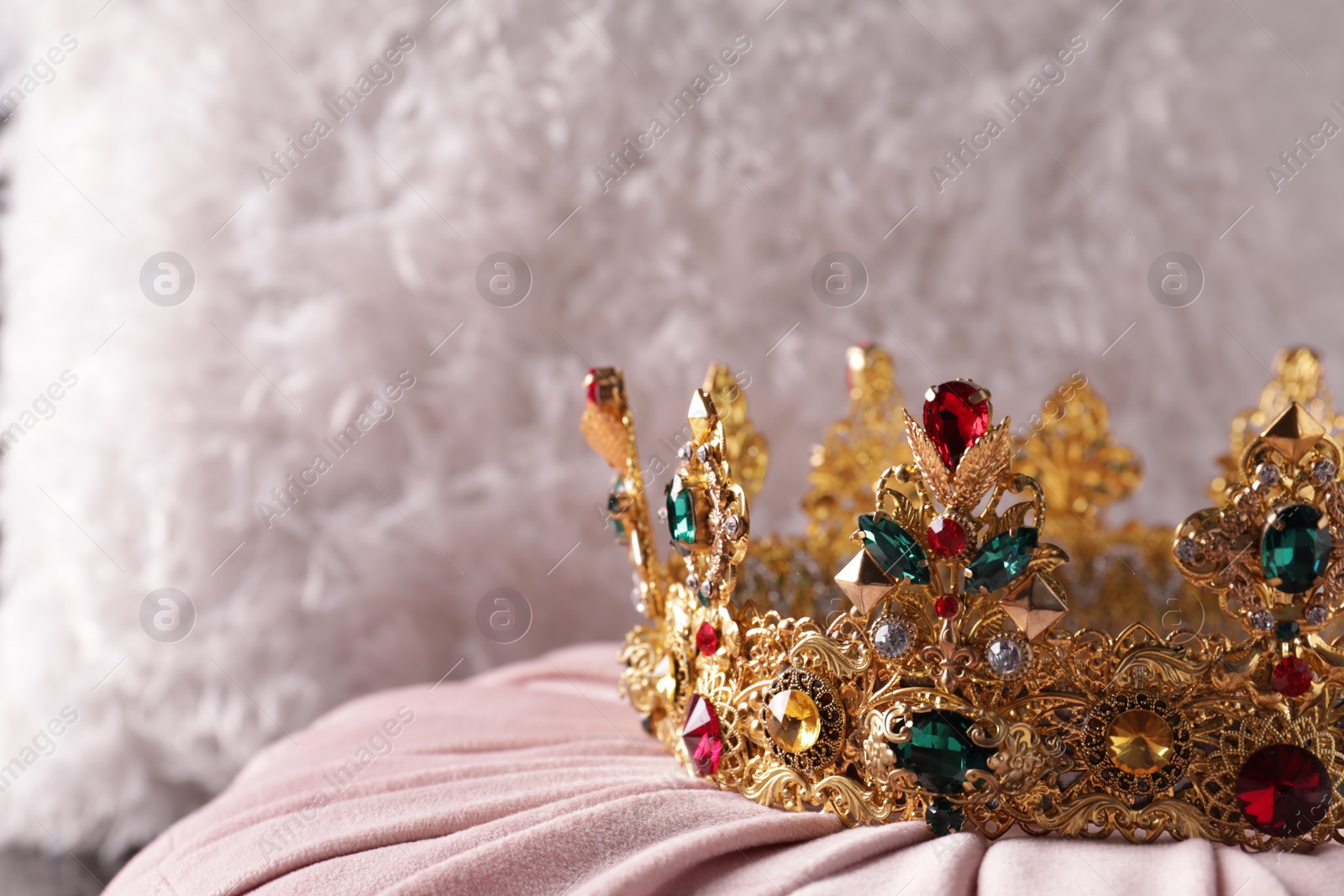 Photo of Beautiful golden crown with gems on pink cloth, closeup. Space for text