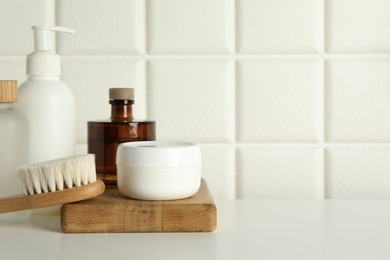Photo of Bath accessories. Personal care products and wooden brush on white table near tiled wall, space for text