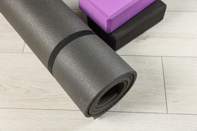 Photo of Exercise mat and yoga blocks on light wooden floor, closeup
