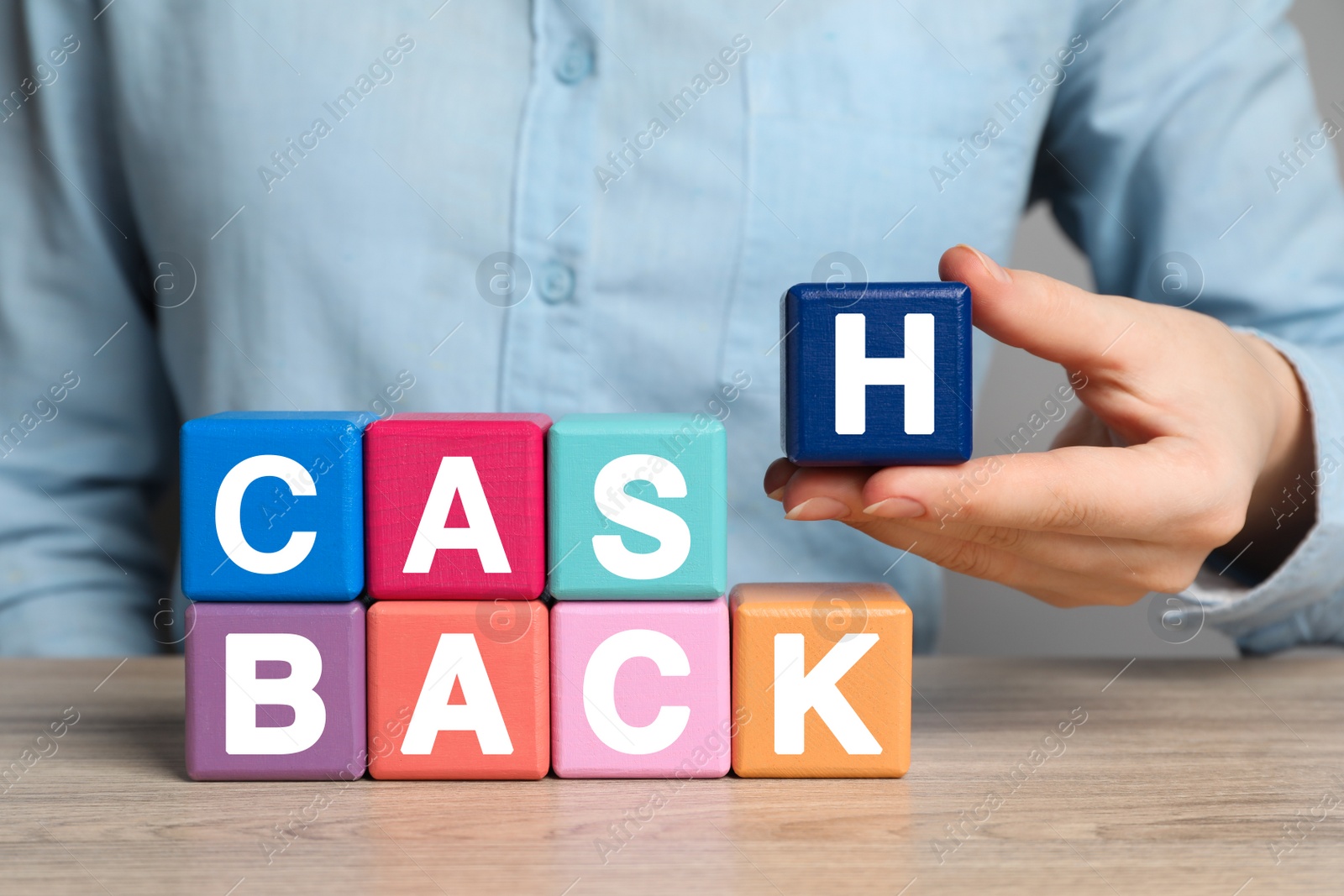 Photo of Woman making word Cashback with colorful cubes at wooden table, closeup