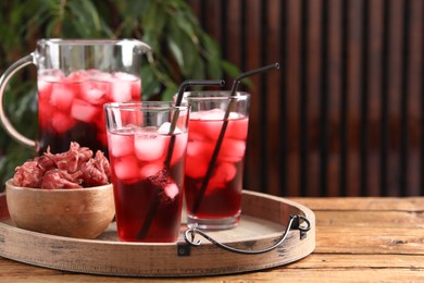 Delicious iced hibiscus tea and dry flowers on wooden table, space for text