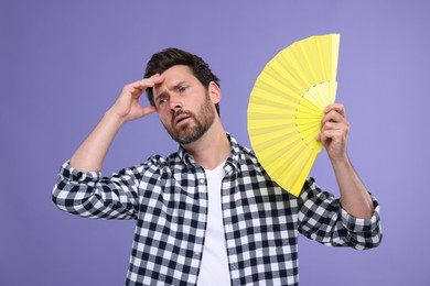 Photo of Unhappy man with hand fan suffering from heat on purple background