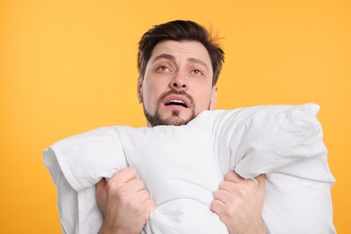 Tired man with pillow on yellow background. Insomnia problem