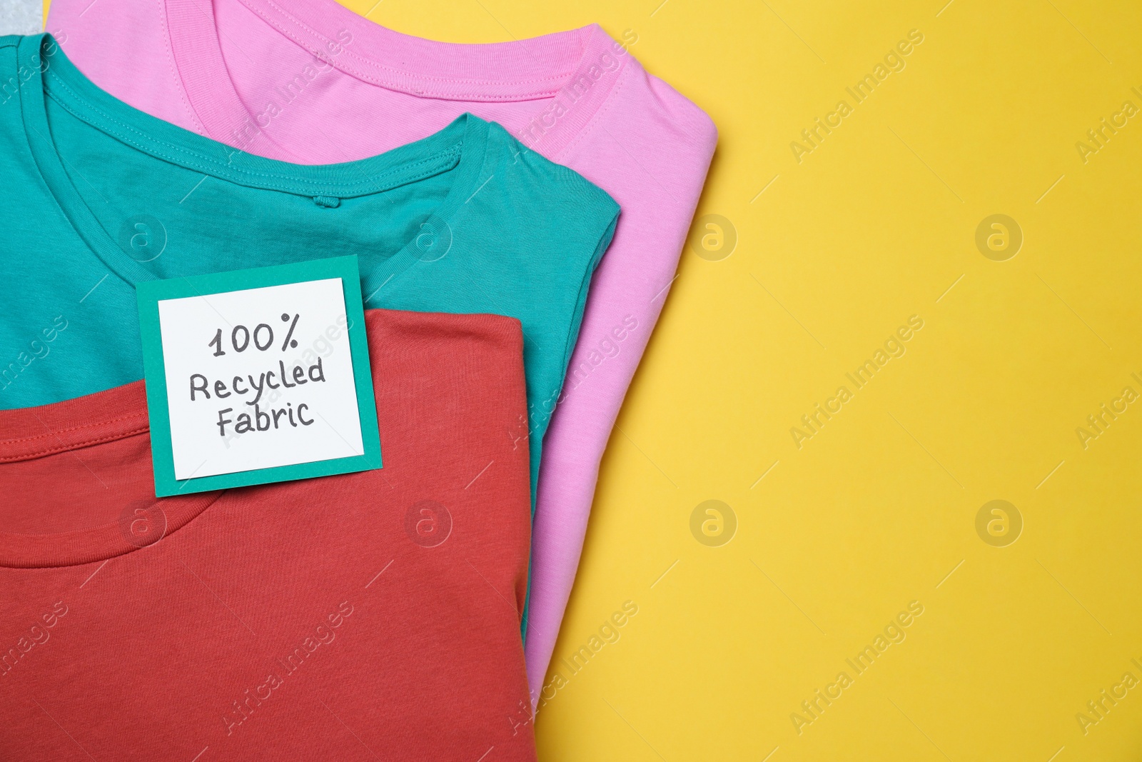 Photo of Different clothes with recycling label on yellow background, top view. Space for text