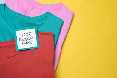 Photo of Different clothes with recycling label on yellow background, top view. Space for text