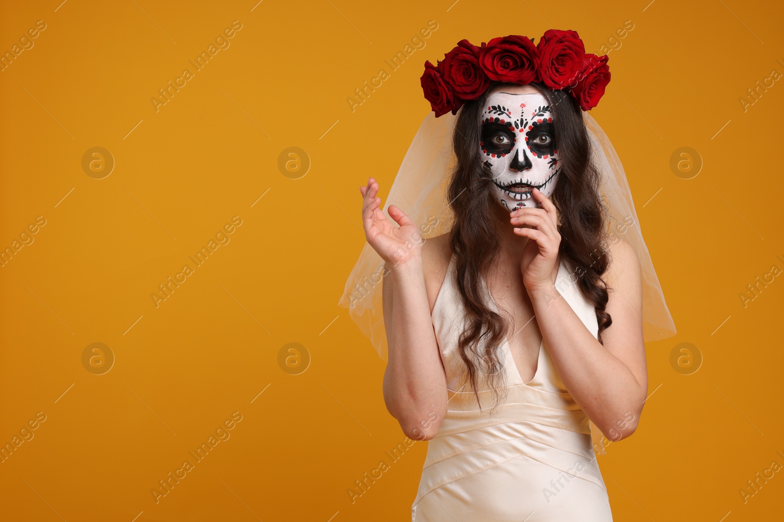 Photo of Young woman in scary bride costume with sugar skull makeup and flower crown on orange background, space for text. Halloween celebration