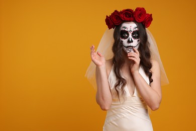 Young woman in scary bride costume with sugar skull makeup and flower crown on orange background, space for text. Halloween celebration