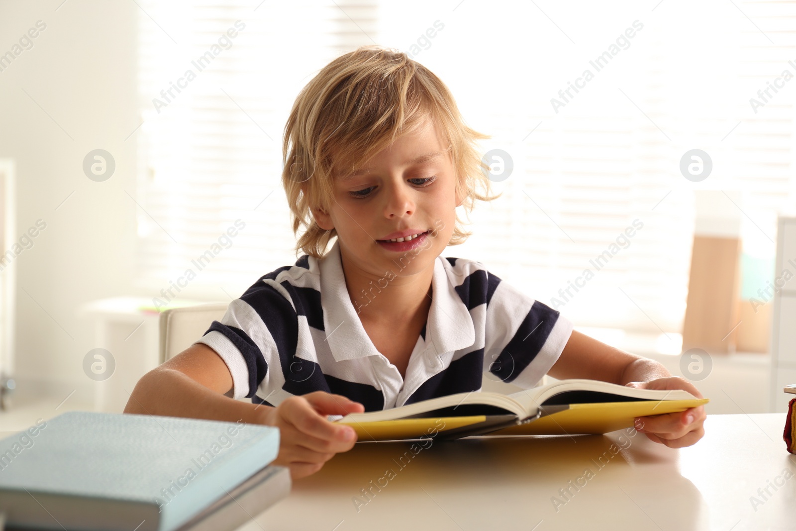 Photo of Little boy doing homework at table indoors