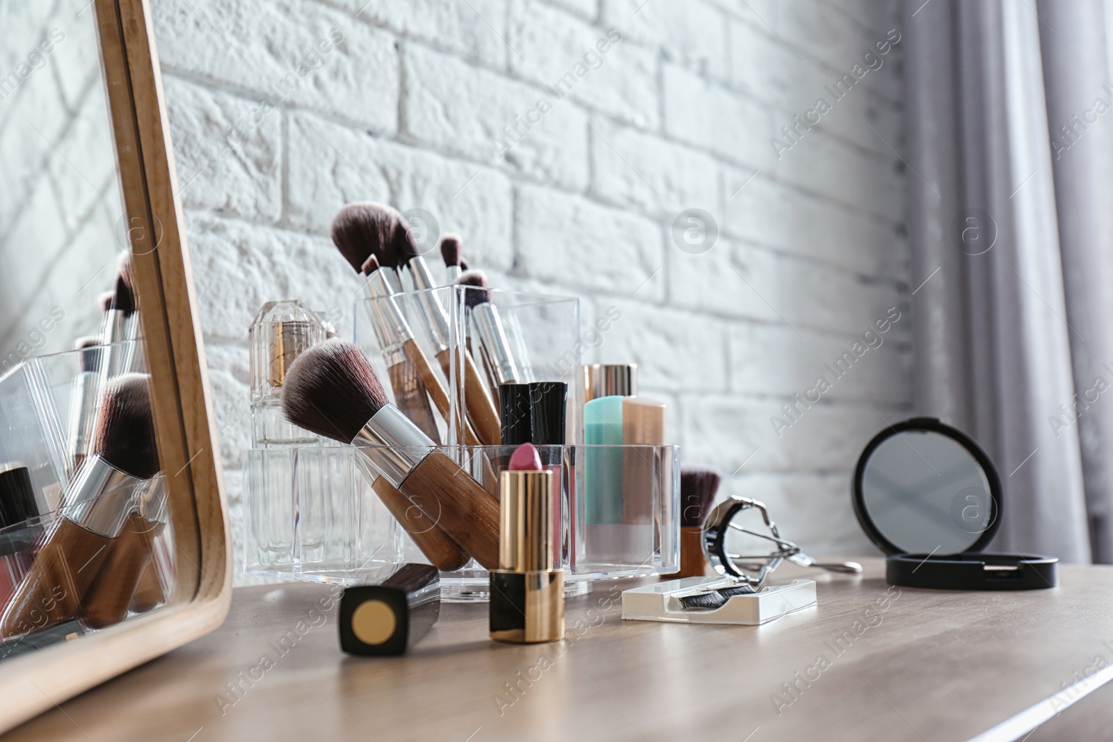 Photo of Organizer with cosmetic products for makeup on table near brick wall