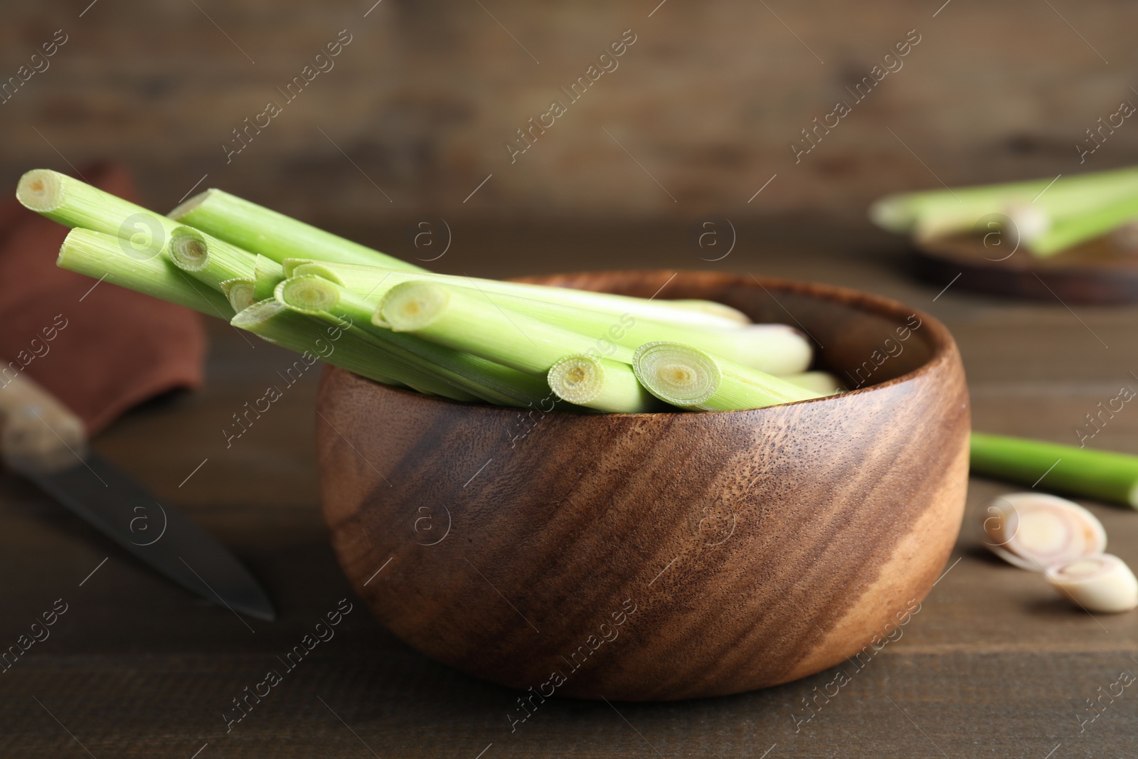 Photo of Bowl with fresh lemongrass stalks on wooden table, closeup