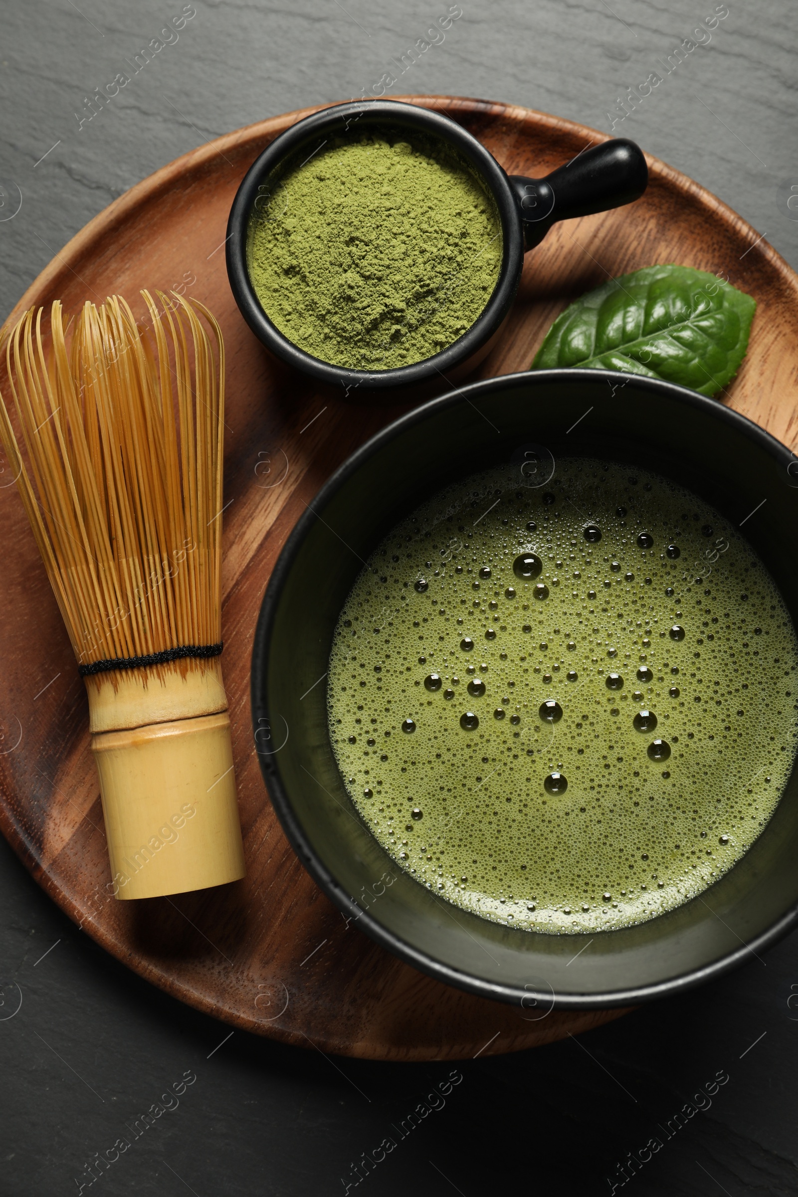 Photo of Cup of fresh matcha tea, bamboo whisk and green powder on black table, top view