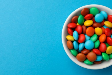 Photo of Bowl with tasty colorful candies on blue background, top view. Space for text