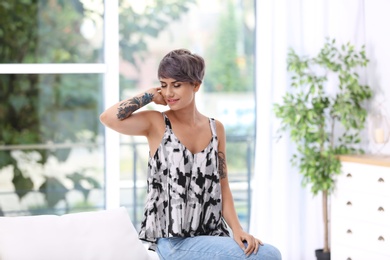 Photo of Trendy young woman with tattoos on sofa indoors