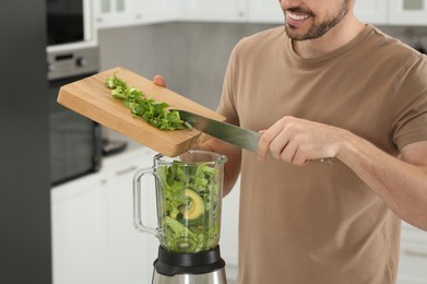 Photo of Man adding cut spinach for delicious smoothie in kitchen, closeup