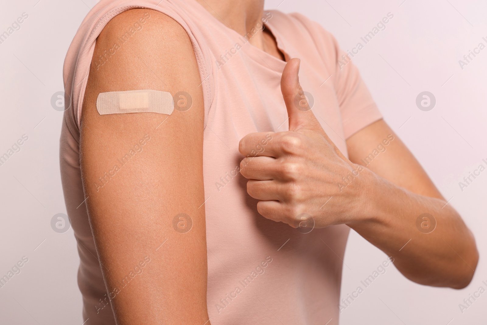 Photo of Woman with adhesive bandage on arm after vaccination showing thumb up on light background, closeup