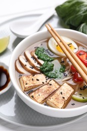 Delicious vegetarian ramen in bowl and chopsticks on white table, closeup