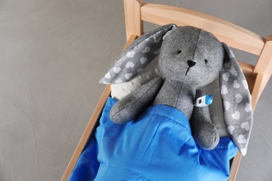 Toy bunny with thermometer lying in bed on grey background, top view. Children's hospital