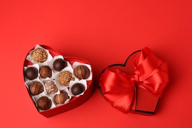 Photo of Heart shaped box with delicious chocolate candies on red table, above view. Space for text