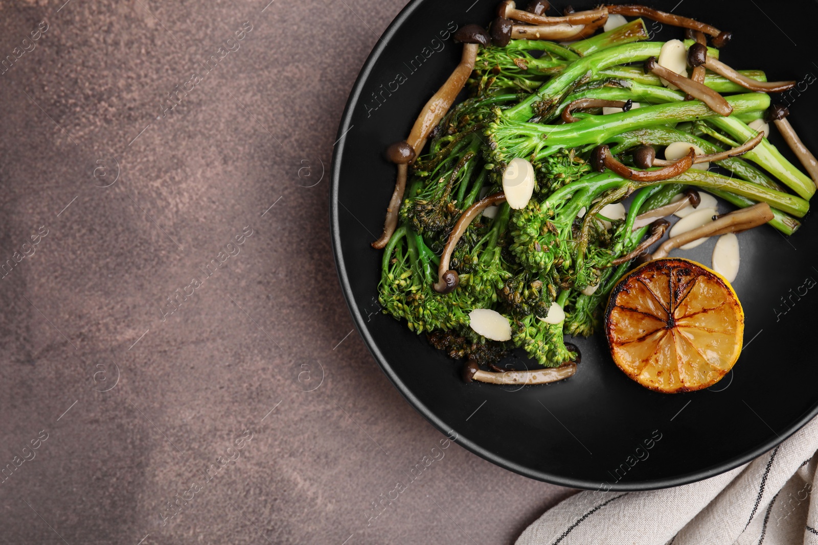 Photo of Tasty cooked broccolini with lemon and mushrooms on grey table, top view. Space for text