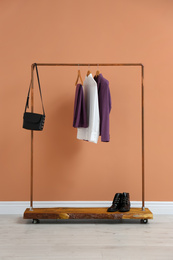 Rack with stylish women's clothes and boots near color wall
