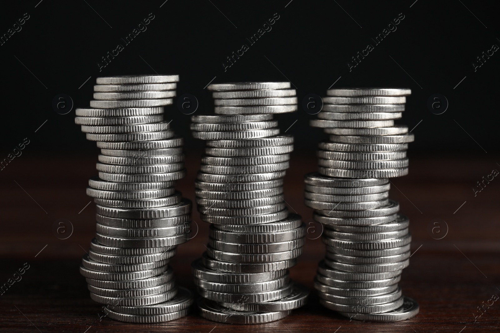 Photo of Many coins stacked on wooden table against black background