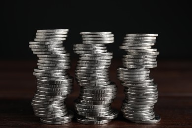 Many coins stacked on wooden table against black background