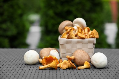 Photo of Different fresh mushrooms and basket on grey rattan table outdoors, space for text