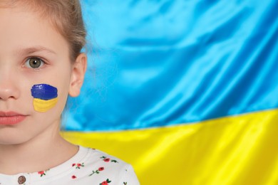 Photo of Little girl with face paint near Ukrainian flag, closeup. Space for text