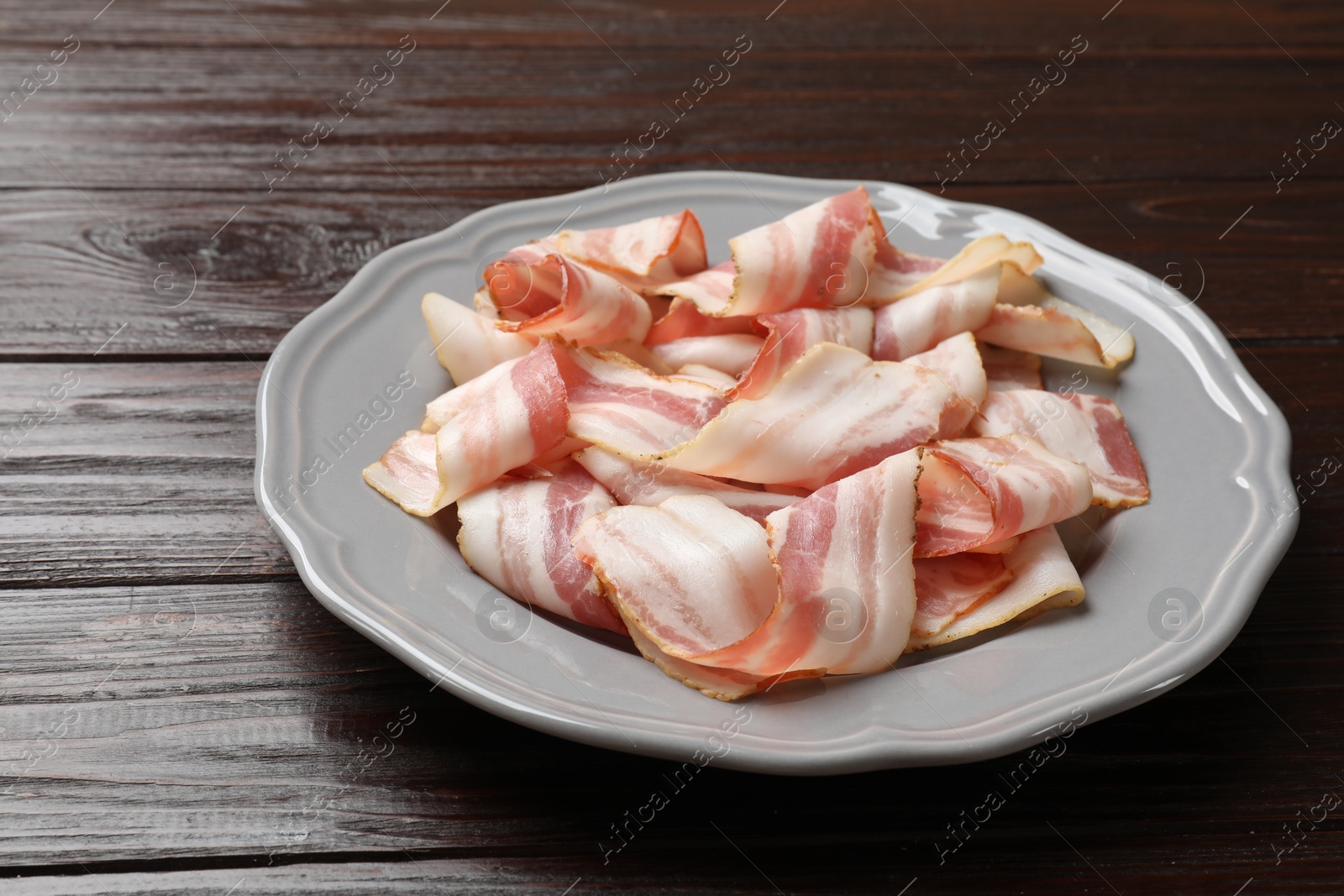 Photo of Slices of raw bacon on dark wooden table, closeup