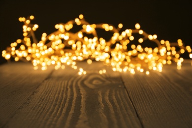 Photo of Beautiful glowing Christmas lights on wooden surface, blurred view