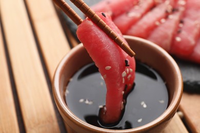 Photo of Dipping tasty sashimi (piece of fresh raw tuna with sesame seeds) into soy sauce at table, closeup