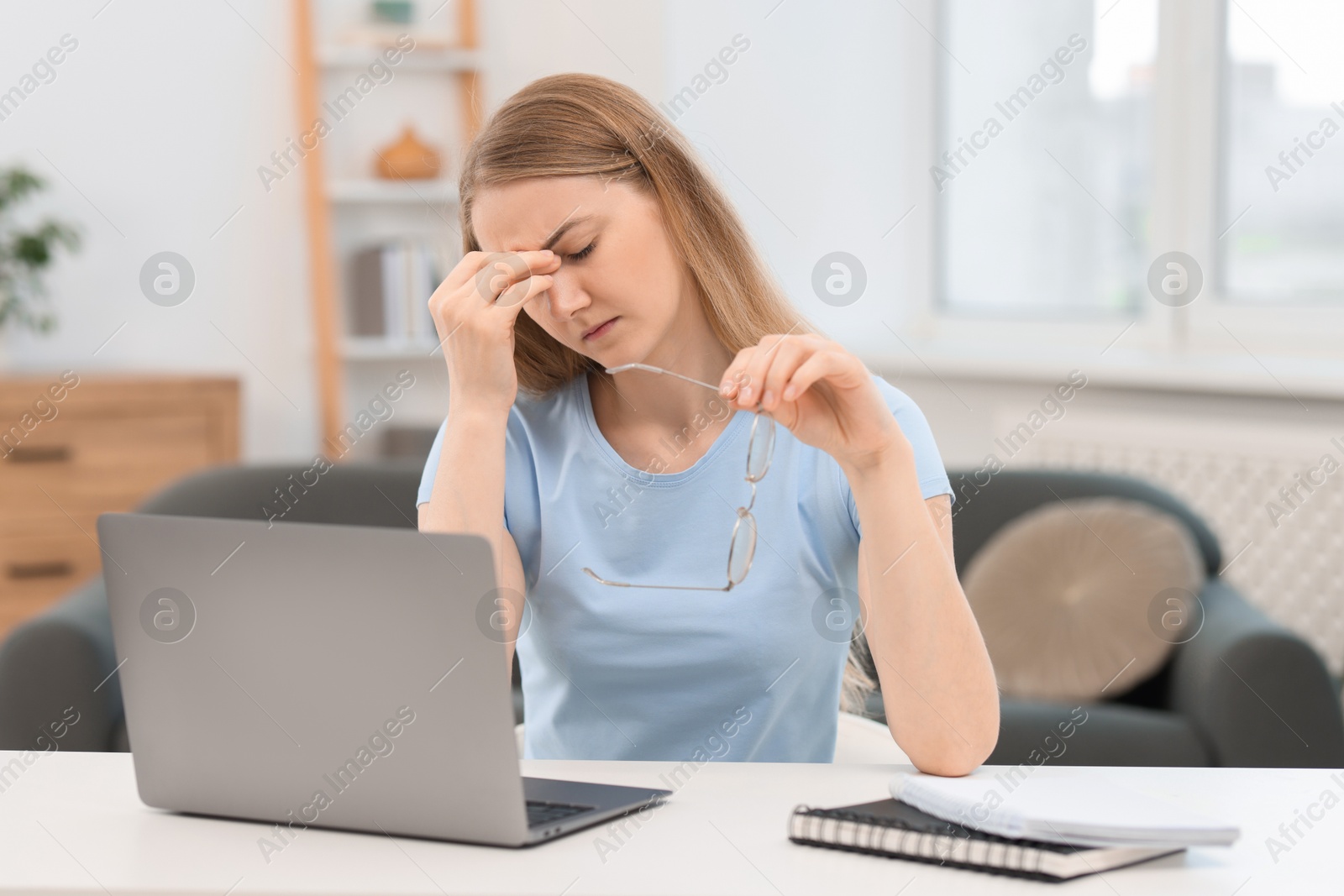 Photo of Overwhelmed young woman sitting with laptop at table in room