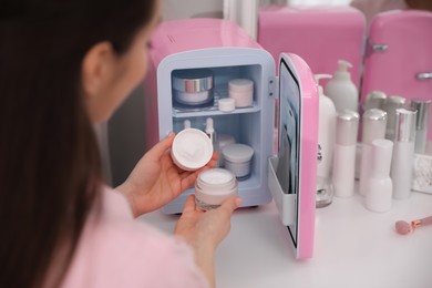 Woman taking cosmetic product out of mini refrigerator indoors, closeup