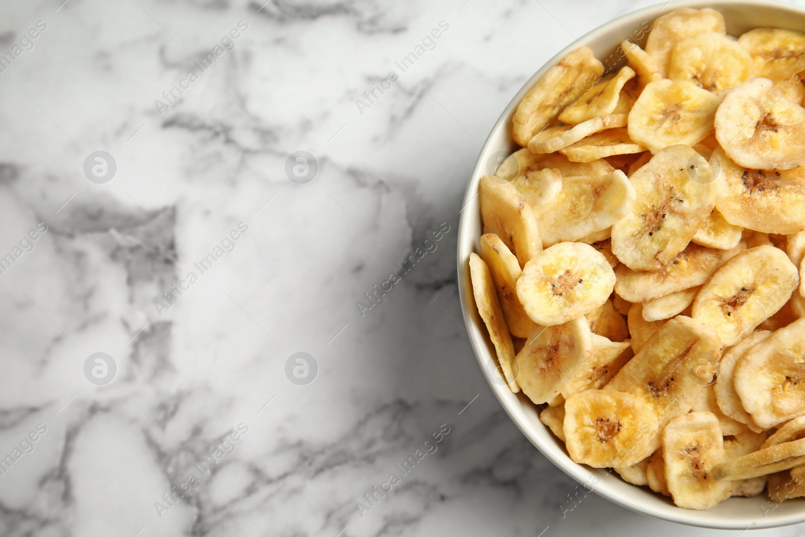 Photo of Bowl with sweet banana slices on marble background, top view with space for text. Dried fruit as healthy snack